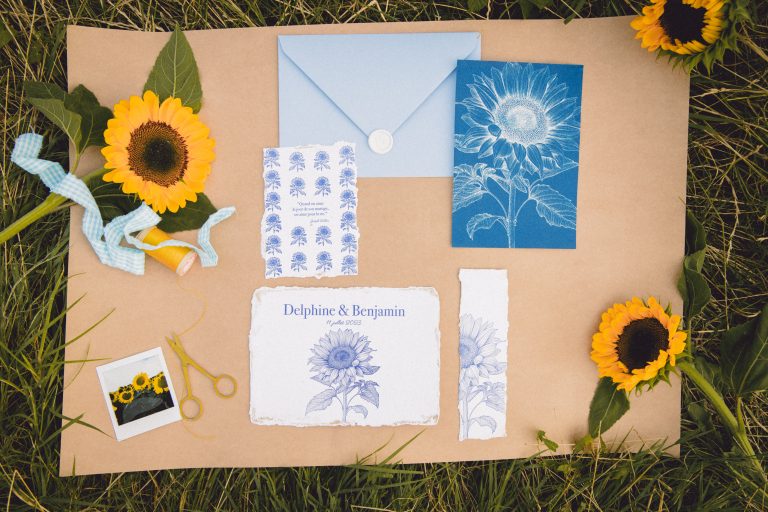 Papeterie de mariage avec tournesol et éléments bleus sur fond naturel.