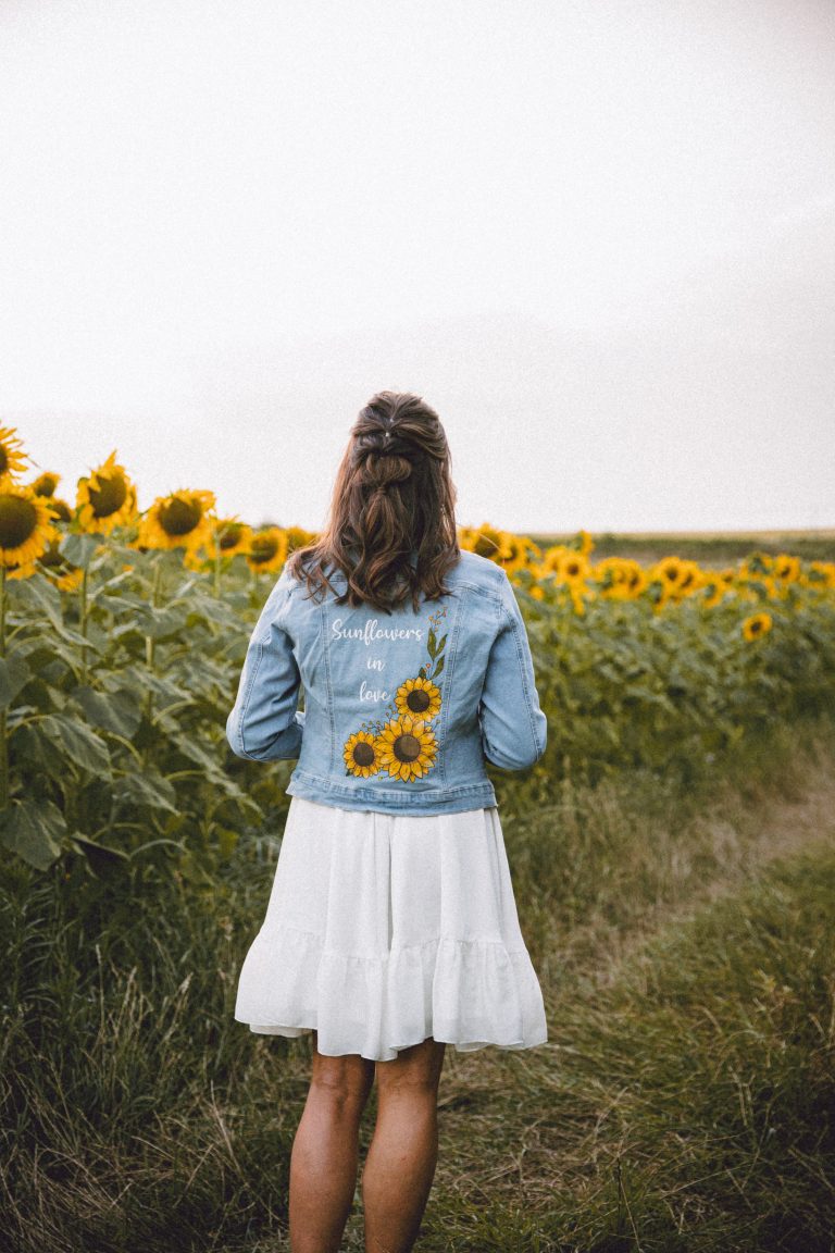 Femme de dos regardant un champ de tournesols, vêtue d'une veste en jean brodée.