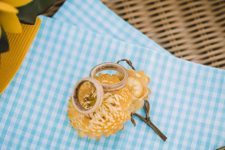 Anneaux de mariage en bois posés sur une fleur jaune, présentation sur tissu à carreaux.