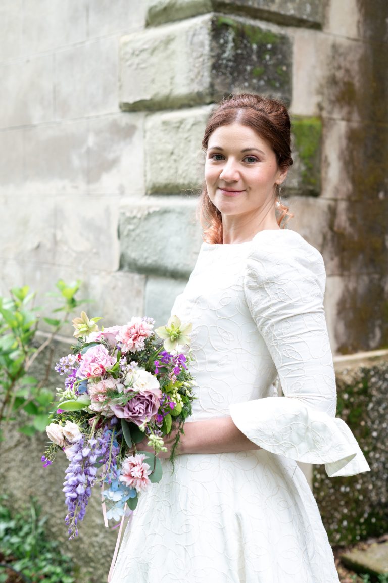 Mariée souriante tenant un bouquet coloré devant un mur de pierre