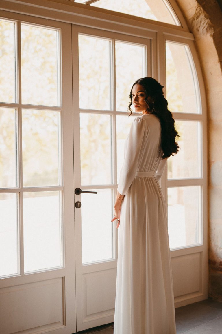 Mariée en robe blanche regardant par la fenêtre