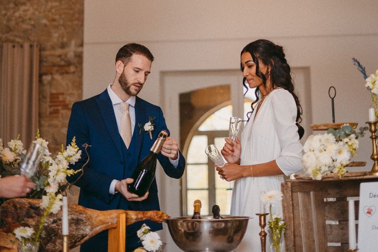 Le marié ouvre une bouteille de champagne tandis que la mariée tient deux verres.