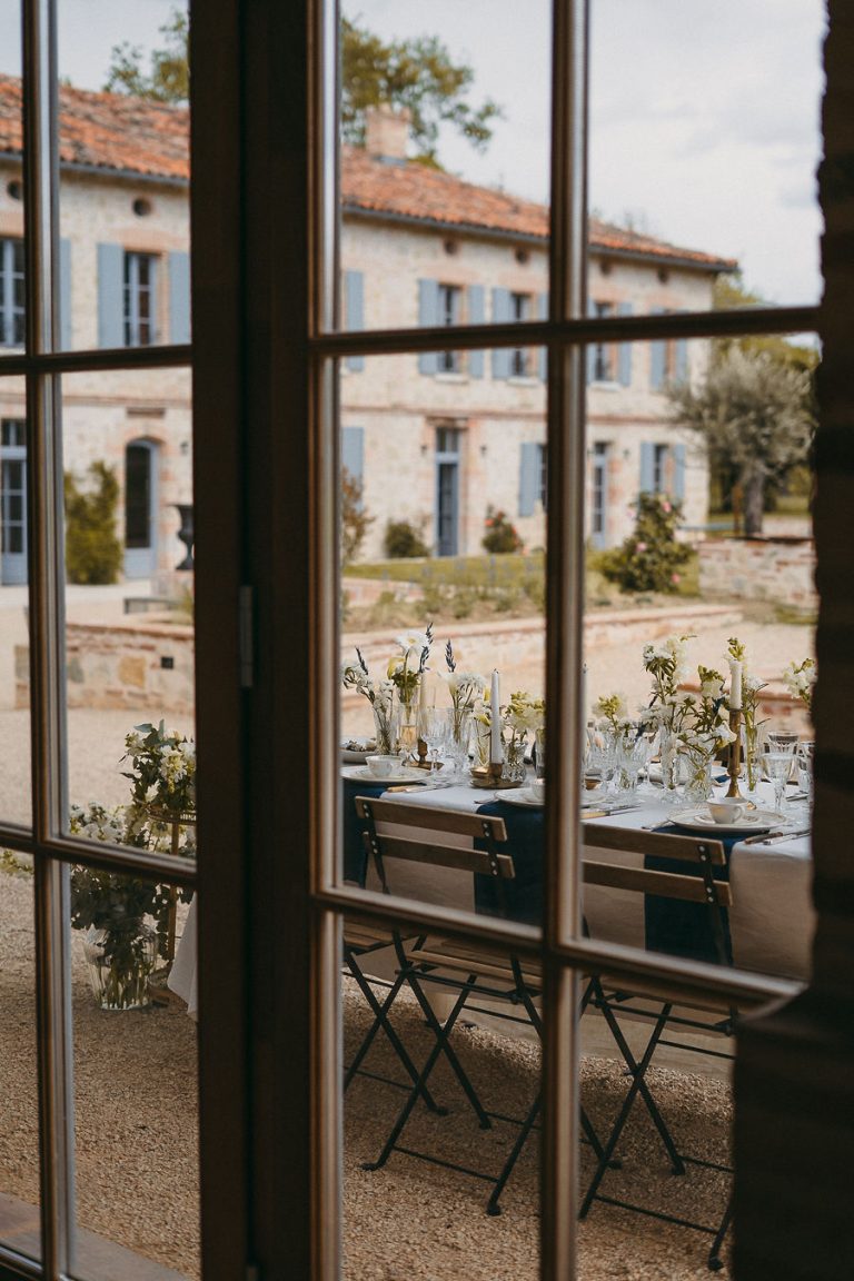 Table de réception vue à travers une fenêtre, décorée de fleurs blanches