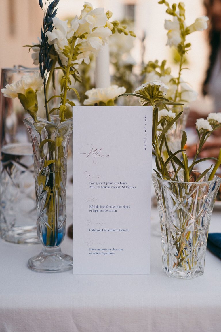 Menu de mariage sur une table décorée avec des fleurs blanches et des verres en cristal