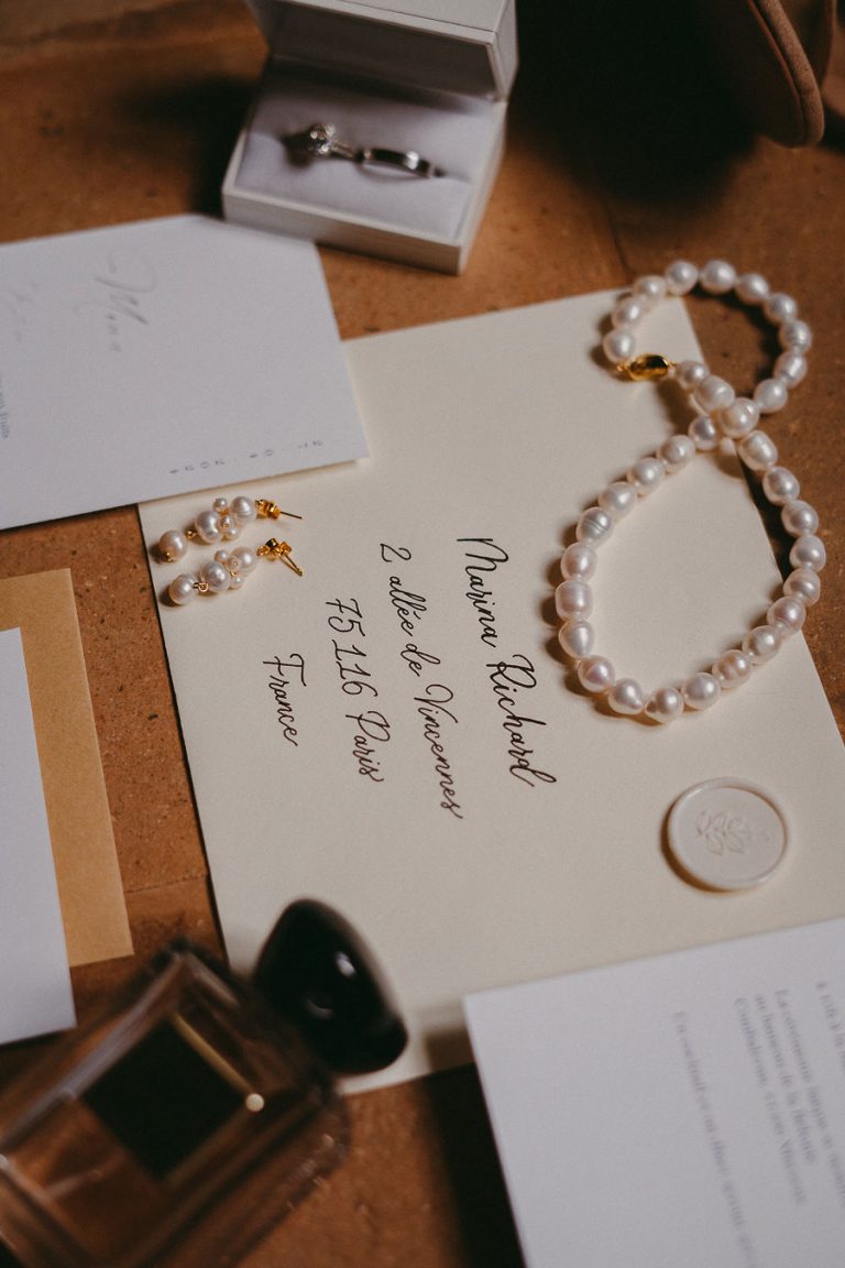 Détails de la papeterie de mariage avec une bague et un collier de perles