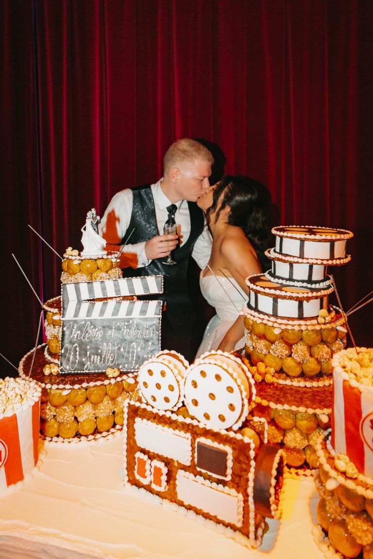 Mariés célébrant leur mariage avec un gâteau cinéma dans une ambiance festive et colorée.