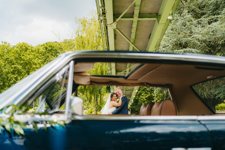 Couple de mariés souriant à travers la fenêtre d’une voiture ancienne.