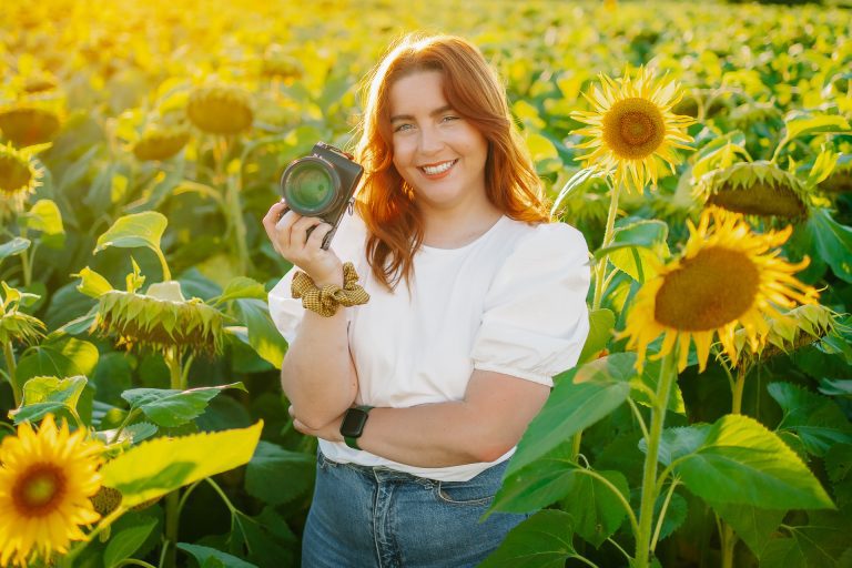 Laura Vergne, photographe mariage, souriante dans un champ de tournesols avec son appareil photo en main.