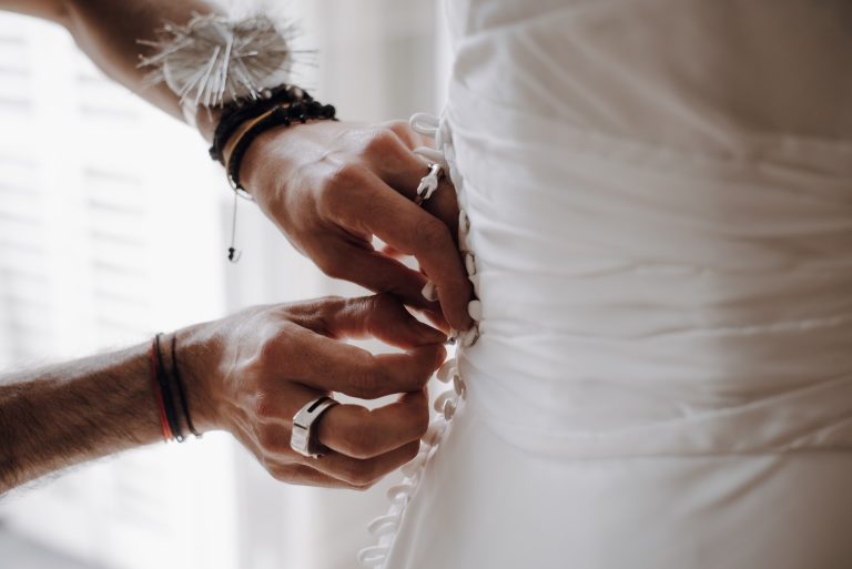 Gros plan sur les mains d’un créateur ajustant les boutons d’une robe de mariée.