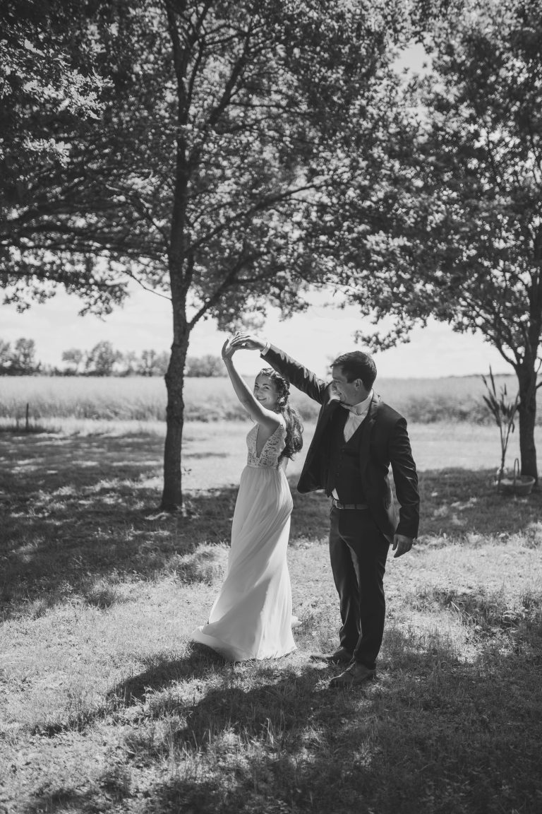 Style photo mariage noir et blanc : Les mariés dansant sous les arbres dans une ambiance naturelle et intemporelle.