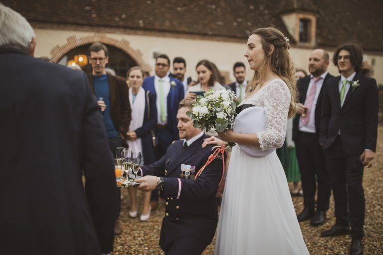 Style photo mariage : Le marié en uniforme servant des boissons pendant le vin d’honneur.