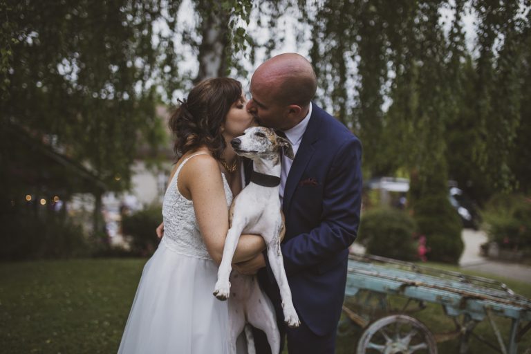 Style photo mariage dark and moody : Les mariés partageant un baiser avec leur chien dans un cadre naturel et intime.