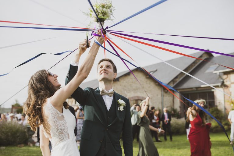 Style photo mariage lifestyle : Les mariés coupant des rubans colorés lors d’un jeu traditionnel en extérieur.