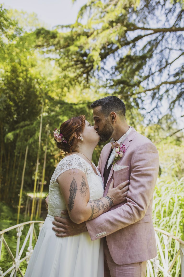 light and airy : Mariés échangeant un baiser sur un pont dans un cadre naturel baigné de lumière.