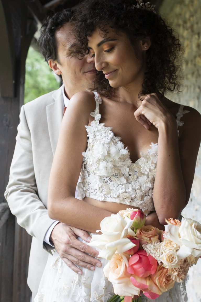 Style photo mariage éditorial : Les mariés dans une pose élégante, avec une robe en dentelle et un bouquet de fleurs pastel.